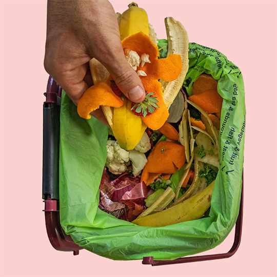 A hand reaching over a food waste bin and dropping in a handful of fruit peels and skin.